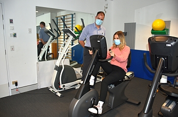 A woman seated on an excercise machine while being supervised by an clinican